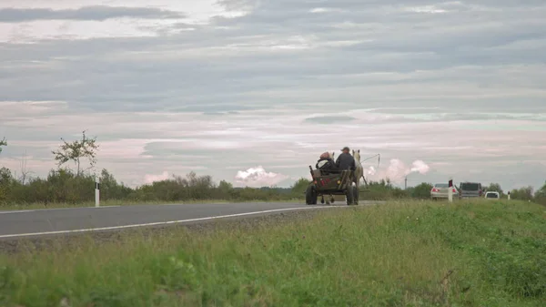 Sur la nouvelle route après réparation paysans vont sur les feux et les chevaux, vieux transports, les pauvres sur les transports sont dépassés par les voitures modernes, les gens hors de la civilisation moderne — Photo