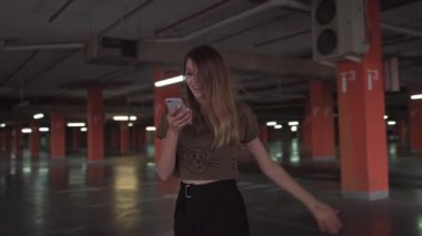Şanslı bir genç kız telefona bakar ve telefondaki iyi haberi görür. Kadınlar sevinir, güler, zıplar. 4K RAW yeraltı otoparkında ateş edildi.