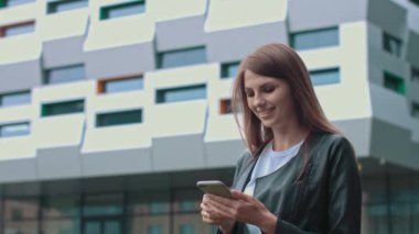 Uzun esmer saçlı çekici bir kız sokakta yürüyor, ellerinde cep telefonu var. Mesaj yazmak ve gönderirken gülümsemek. Modaya uygun kıyafetleri var..