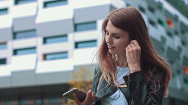 Çekici kız, öğrenci, modern giysiler içinde iyi ruh hali müziği dinlemek için bir cep telefonu kullanıyor, müzik aşığı favori bir şarkı koyuyor, mutlu kadın gezinti yapıyor, yüksek hız bağlantısı 5G