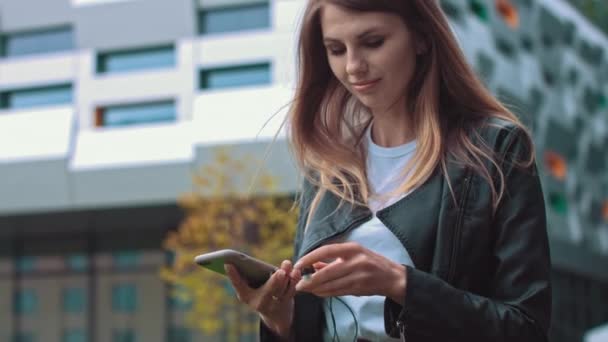 Atrakcyjna dziewczyna, studentka, w nowoczesnych ubraniach Używa telefonu komórkowego do słuchania dobrej muzyki nastroju, meloman stawia ulubioną piosenkę, szczęśliwa kobieta korzysta z roamingu, szybkie połączenie 5G — Wideo stockowe