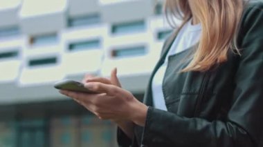 Modern bir binanın arka planında şık giyinmiş çekici genç bir kız telefona bakar ve bir mesaj yazar. İşaret parmağınla havaya dokun. İnternetten alışveriş. Kız bir...
