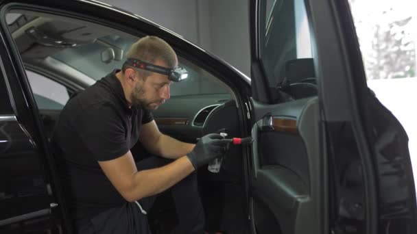 The man treats the interior of the car with an antibacterial agent, cleaning the cracks of the car door with a brush, detailed cleaning of the car interior — Stock Video