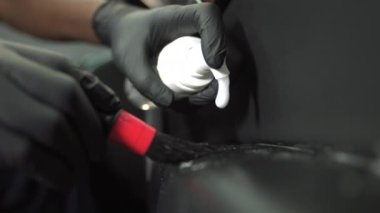 Afro-Amerikalı bir erkeğin ellerine yakın çekim, bakteriden bir fırça ve köpükle temizlik, arabanın zeminini kurtarmak, deri iç kısımları korumak, kimyasalları yüzeye uygulamak.