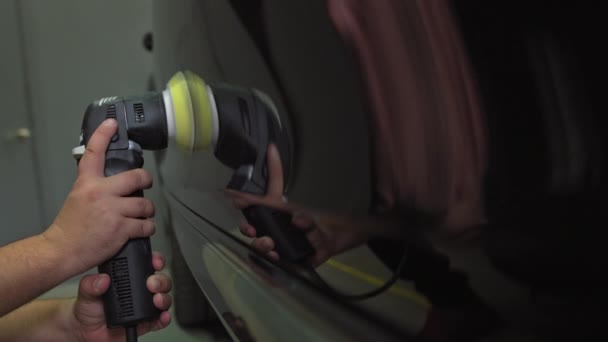 男性の自動車整備士は、傷を除去するための研磨機で黒い車のボディを研磨します。4kの解像度で撮影. — ストック動画