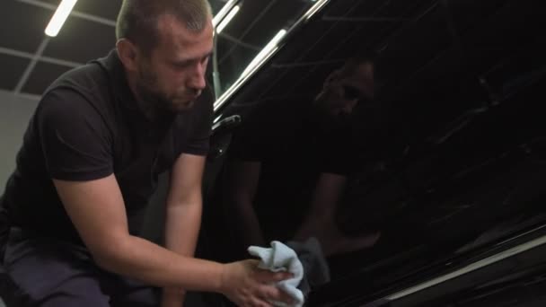 一名男性汽车修理工在恢复尸体后用微型纤维擦拭一辆黑色汽车。抛光汽车零部件 — 图库视频影像