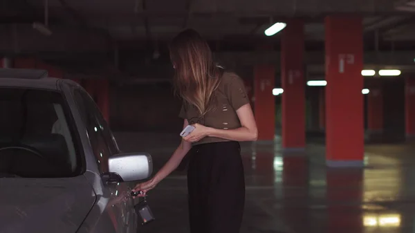 Uma mulher atraente usa uma chave para abrir um carro em um estacionamento subterrâneo. Uma menina bonita abre o carro. — Fotografia de Stock