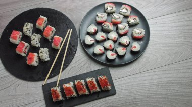Japon yemek kompozisyonu. Siyah taş tahtaya çeşitli suşi çeşitleri konmuş. Baharatlı kimçi salatası, wonton çorbası, yemek çubukları ve soya sosu kasesi..