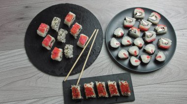 Japon yemek kompozisyonu. Siyah taş tahtaya çeşitli suşi çeşitleri konmuş. Baharatlı kimçi salatası, wonton çorbası, yemek çubukları ve soya sosu kasesi..