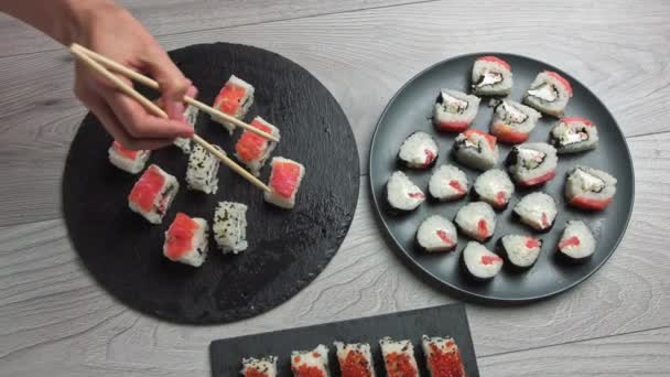 Ženská ruka si bere jídlo hůlkami. Japonské složení jídla. Různé druhy sushi umístěné na černé kamenné desce. pikantní kimchi salát, wontonová polévka, hůlky a sójová omáčka. — Stock video