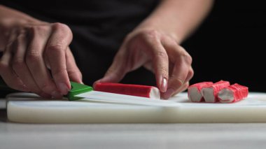 Kadın elleri evdeki mutfakta salatalıklı mısır yumurtasından salata yapar. Kadın salataya yengeç dilimleri kesiyor.