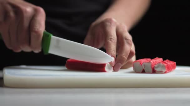 Ženské ruce dělají salát z krabích tyčinek okurkové kukuřičné vejce v kuchyni doma. Žena krájí krabí tyčinky do salátu — Stock video