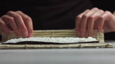 Suşi şefi lezzetli suşi ruloları için Norveç çarşafına Japon suşi pilavı seriyor. - Yüksek açılı atış.