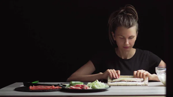 Lo chef in guanti sta cucinando il sushi maki usando il tappetino. I Maki sono fatti di riso, alghe nori, cetrioli, crema di formaggio. Cibo giapponese appetitoso e nutriente. — Foto Stock