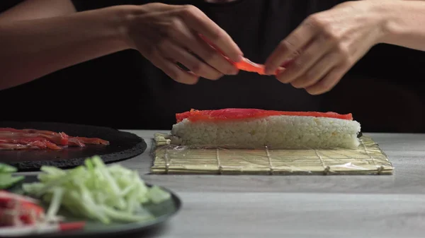 Le chef japonais prépare des rouleaux de sushi avec du saumon et de l'avocat. Cuire les mains en faisant rouler les sushis japonais sur le tapis de bambou. Délicieux plats japonais, vue à faible angle — Photo