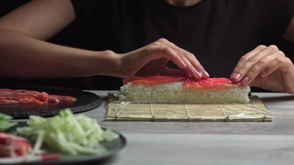日本厨师用鲑鱼和鳄梨做寿司卷.煮手,使日本寿司滚在竹席上.味道鲜美的日本菜，低视角 — 图库照片