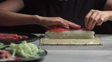 Japon şef somon ve avokadoyla suşi ruloları hazırlar. Japon suşisini bambu hasırında pişiren el yapımı. Lezzetli Japon yemekleri, düşük açı manzaralı.