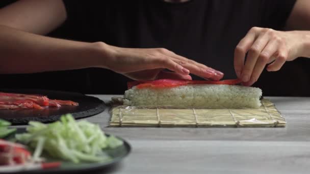 Japonský kuchař připravuje sushi rolky s lososem a avokádem. Vařit ruce dělat japonské sushi rolku na bambusové rohoži. Lahodné japonské jídlo, nízkoúhlý pohled — Stock video