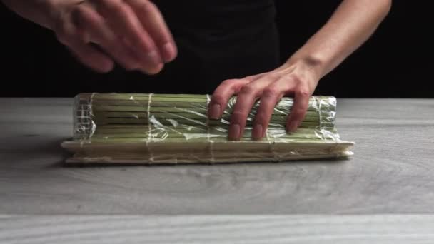 Lo chef in guanti sta cucinando sushi maki usando stuoia. I Maki sono fatti di riso, alghe nori, cetrioli, crema di formaggio. Cibo giapponese appetitoso e nutriente. — Video Stock