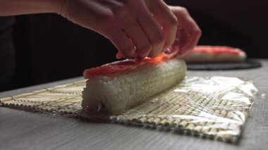 Otantik Japon restoranında çalışırken taze suşi ve bambu hasırıyla kesilmiş isimsiz aşçı elleri bambu matı üzerinde suşi rulosu saran şeflerin yakın çekimi.