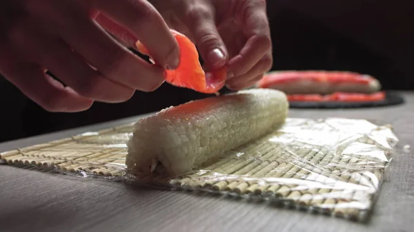 本格的な日本料理店で働きながら、竹のマットで新鮮な寿司を転がしながら匿名の料理人の手を切り、竹のマットで寿司ロールを転がします。寿司作りプロセス — ストック写真