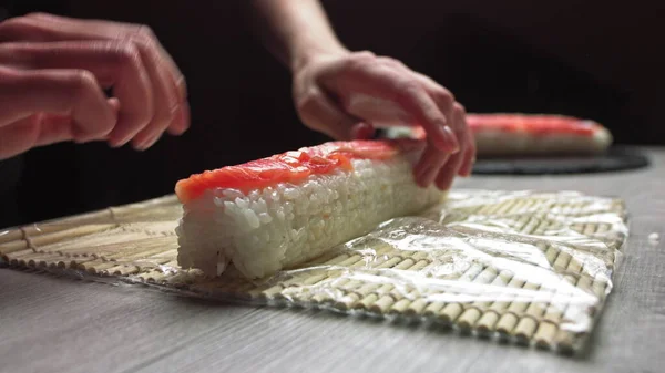 在日本正宗餐馆工作时，用竹子垫滚动新鲜寿司的匿名厨师手，用竹子垫滚动寿司卷的厨师手。寿司制作过程 — 图库照片