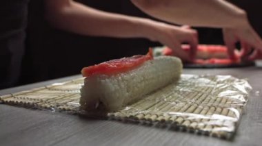 Otantik Japon restoranında çalışırken taze suşi ve bambu hasırıyla kesilmiş isimsiz aşçı elleri bambu matı üzerinde suşi rulosu saran şeflerin yakın çekimi.