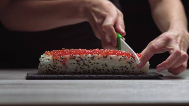 Şef, suşi maki 'yi keskin bıçakla parçalara ayırıyor. Suşi pişirme, hazırlanma süreci. Japon mutfağı..