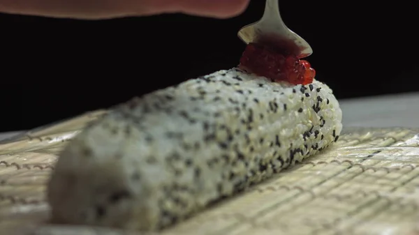 Chef Putting Roe red Sushi Caviar On Top Of Shrimp Tempura Sushi Roll With Avocado Slices Using A Teaspoon - close up, panning shot — стокове фото