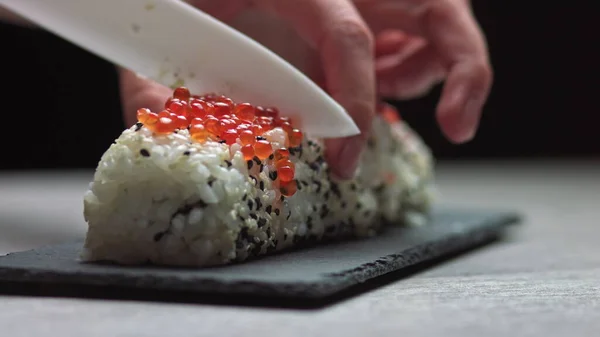 厨师切寿司卷与刀在石板上。-低角度射击。美丽的女性手切割寿司. — 图库照片