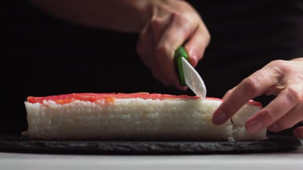 Ο σεφ κόβει ρολά σούσι με ένα μαχαίρι σε μια πέτρινη σανίδα. - πυροβολημένος σε χαμηλή γωνία. Όμορφα γυναικεία χέρια κόβουν σούσι. — Αρχείο Βίντεο