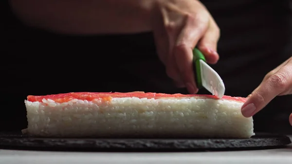 厨师切寿司卷与刀在石板上。-低角度射击。美丽的女性手切割寿司. — 图库照片