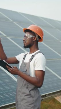 A technician in an orange hard hat inspects solar panels, ensuring efficient energy production.