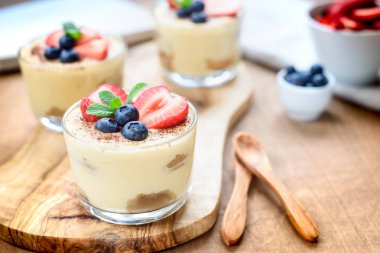 Gözlüklü ev yapımı, enfes tatlı tiramisu çilek, yaban mersini, nane ile dekore edilmiş beyaz tahta masada görünümü top.