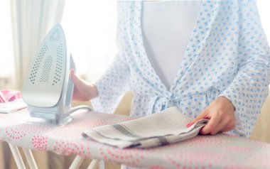 Ütü masasında giysileri ütüleyen bir kadın.