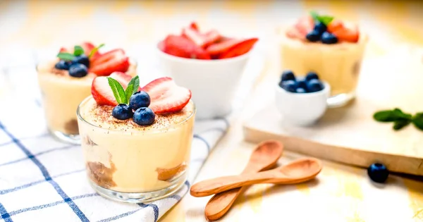 Hecho en casa, exquisito postre tiramisú en vasos decorados con fresa, arándanos, menta en mesa de madera blanca, vista superior . —  Fotos de Stock