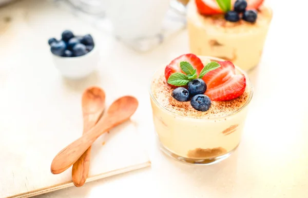 Caseiro, requintado tiramisu sobremesa em óculos decorados com morango, mirtilo, hortelã na mesa de madeira branca, vista superior . — Fotografia de Stock