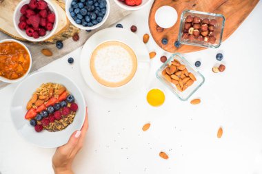 Üstten Görünüm gösteren eller, bal fındık ile yulaf lapası yemek yaban mersini üzerinde tablo beyaz.