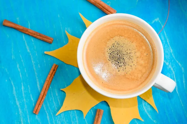 Осенний состав кофе, чашка кофе с пеной, корица, осенний лист на синем фоне. Осенние горячие напитки, концепция кафе и бара — стоковое фото