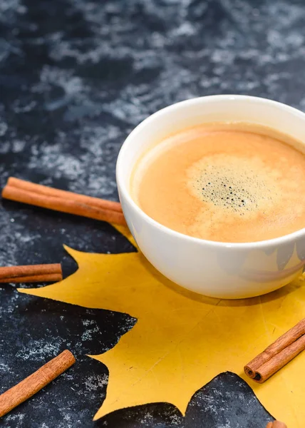 Autumn coffee composition, coffee cup with foam, cinnamon, autumn leaf at black background. Fall hot drinks, cafe and bar concept