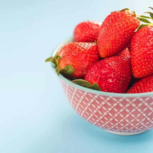 Bunte reife Erdbeeren in einer hellen Schüssel auf blauem Hintergrund — Stockfoto