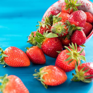 taze parlak çilek mavi bir arka plan üzerinde kase dışarı dökülen