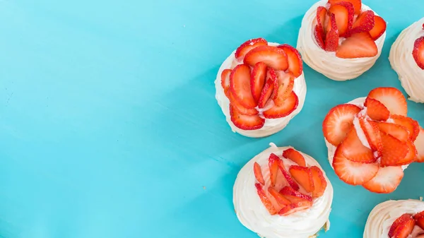 A small meringue Pavlova dessert with some strawberry slices on a blue background. Top view. — Stock Photo, Image