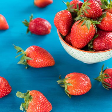 mavi bir arka planda bir kase üst görünümünde taze parlak çilek