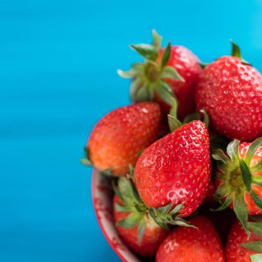 mavi bir arka planda bir kase üst görünümünde taze parlak çilek