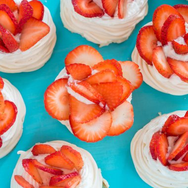 Mavi bir arka plan üzerinde bazı çilek dilimleri ile küçük bir beze Pavlova tatlı. Üstte görüntü.