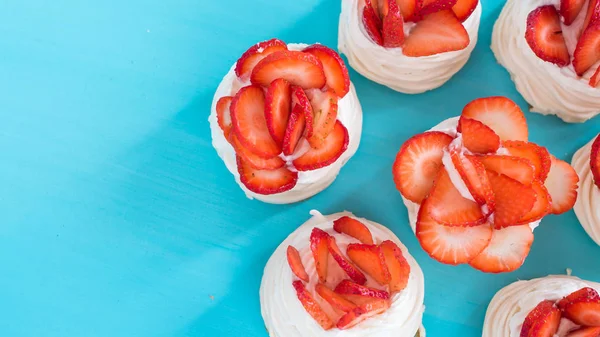 A small meringue Pavlova dessert with some strawberry slices on a blue background. Top view. — Stock Photo, Image