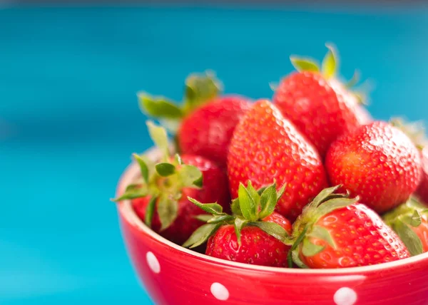 mavi bir arka plan üzerinde parlak bir kapta renkli olgun çilek