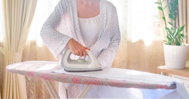 Ütü masasında giysileri ütüleyen bir kadın.