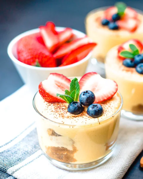 Homemade, exquisite dessert tiramisu in glasses decorated with strawberry, blueberry, mint on black wooden table — Stock Photo, Image